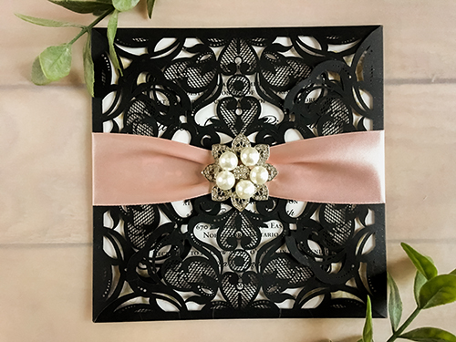 Invitation lc62: This is a four flap laser cut wedding invite in the glittering black color.  There is a deep blush ribbon wrapped around with a 5 pearl rhinestone brooch.