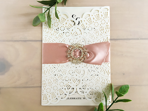 Invitation lc67: Ivory Shimmer, Deep Blush Ribbon, Brooch/Buckle R - This is a fan pattern laser cut wedding invitation in the ivory shimmer color.  There is a deep blush ribbon woven into the brooch design.