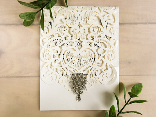 Invitation lc68: Ivory Shimmer, Cream Smooth, Brooch/Buckle A17 - This is an ivory shimmer pocket style laser cut wedding card.  There is a rhinestone brooch glued to the cover flap.