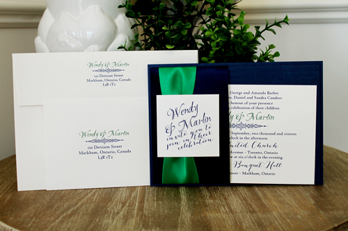 Invitation 1502: This is a navy single pocket invite where the navy pearl paper is folded on the right side to create a pocket which holds the invitation wording card.  A thick emerald ribbon and two navy ribbons are wrapped around the pocket flap.