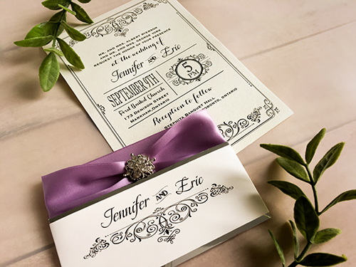 Invitation 1666: White Gold, White Gold, Lavender Ribbon, Brooch/Buckle A8 - This is a single card invite on white gold paper with a silver mirror belly band.  There is a ribbon and brooch design wrapped around.