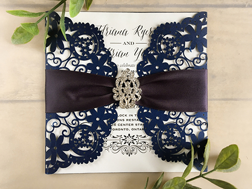 Invitation lc10: Square laser cut invitation, opens with semi-circle gate fold flaps with floral cut out design. Embellished with a deep charcoal ruched ribbon and a brooch, in the center.