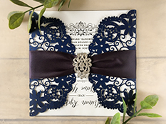 Invitation lc10: Square laser cut invitation, opens with semi-circle gate fold flaps with floral cut out design. Embellished with a deep charcoal ruched ribbon and a brooch, in the center.
