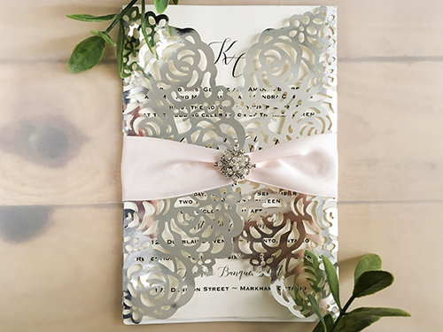 Invitation lc116: This is a silver mirror gate fold laser cut wedding invite.  The flaps have a rose design pattern.  There is a petal pink ribbon and brooch tied around.