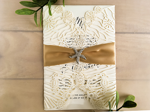 Invitation lc132: Ivory Shimmer, Cream Smooth, Champagne Ribbon, Brooch/Buckle A10 - This is an ivory shimmer laser cut wedding invite that is a gate fold design.  There is a champagne ribbon and brooch wrapped around.