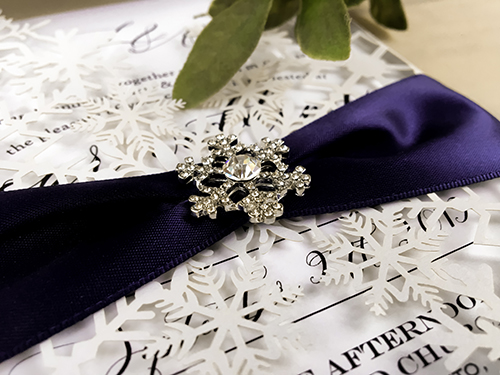 Invitation lc148: White Shimmer, Navy Ribbon, Brooch/Buckle A18 - This is a snow flake inspired white shimmer laser cut invitation design.  It is a gate fold.  There is a navy ribbon and snowflake brooch.