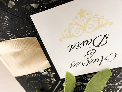 Invitation lc65: Glittering Black, Black Glitter, Cream Smooth, Champagne Ribbon - This is a glittering black four flap laser cut wedding invite.  There is a champagne ribbon tied around with a black glitter cover tag.