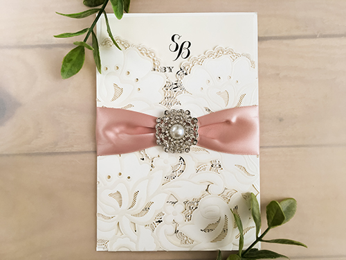 Invitation lc77: Ivory Shimmer, Blush Ribbon, Brooch/Buckle Q - This is an ivory shimmer pocket style laser cut wedding invite.  There is a blush ribbon and pearl brooch.
