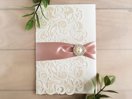 Invitation lc99: Ivory Shimmer, Cream Smooth, Deep Blush Ribbon, Brooch/Buckle G - This is an ivory shimmer laser cut pocket fold wedding invite.  There is a deep blush ribbon and pearl brooch.